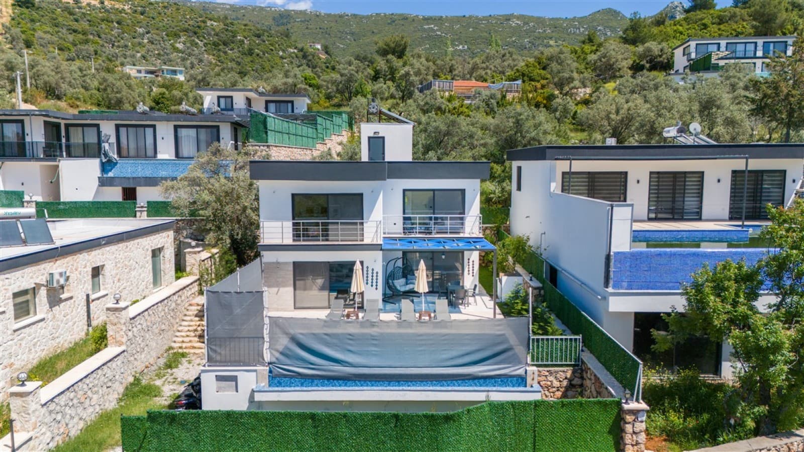 Dağ eteklerinde konumlanmış beyaz cepheli müstakil villa ve havuzu.