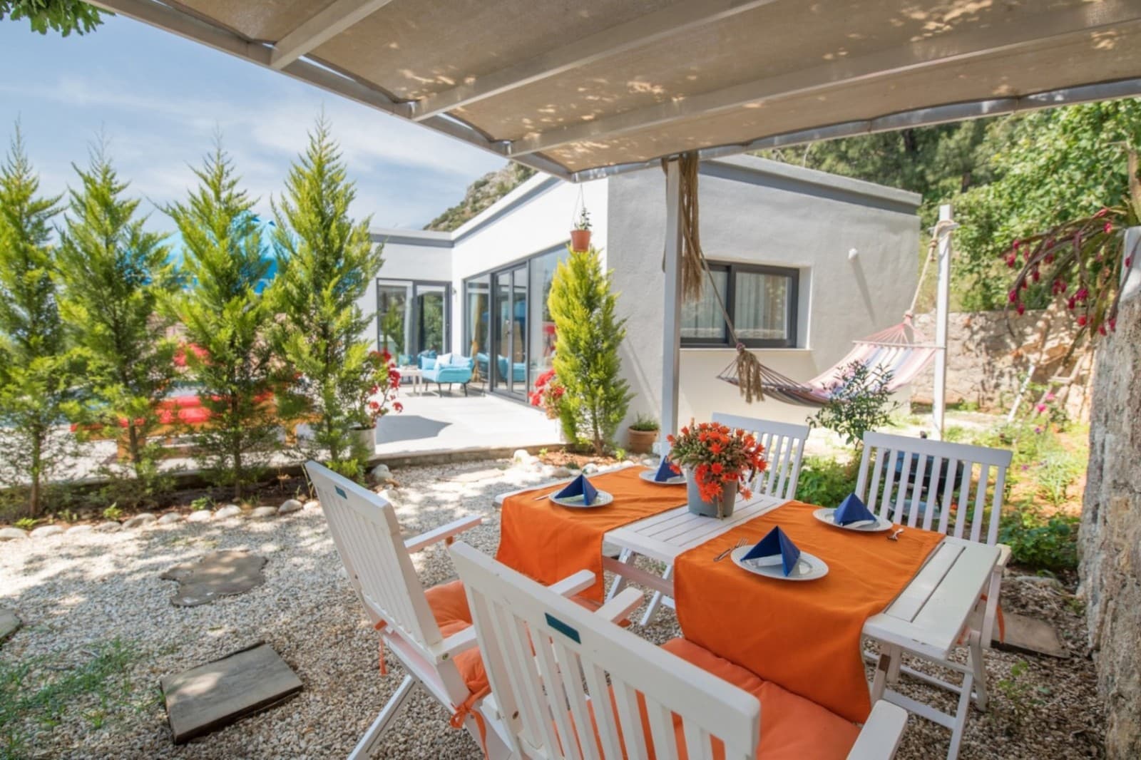 Bahçede turuncu örtülü yemek masası ve hamak bulunan villa dış mekânı.
