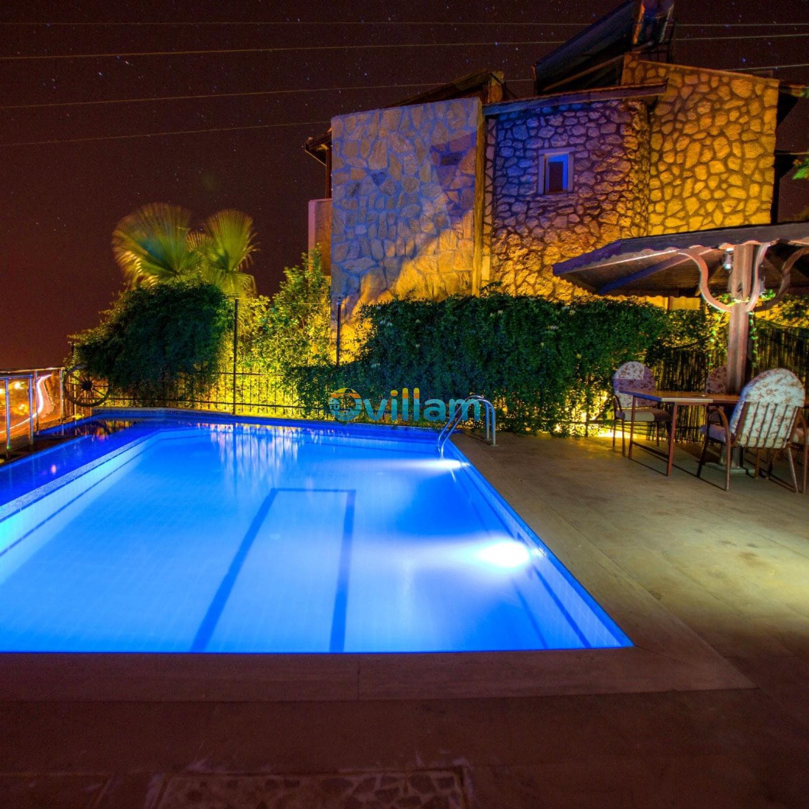 Gece aydınlatılmış taş villa ve havuz alanı.