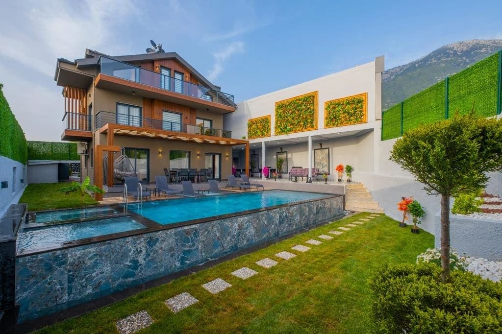Çim alanlı bahçede yer alan modern havuz ve üç katlı villa.