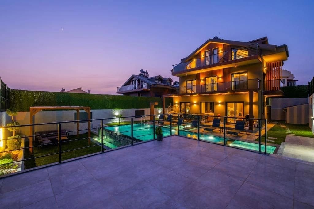 Akşam vakti aydınlatılmış havuz ve villa dış cephesi.