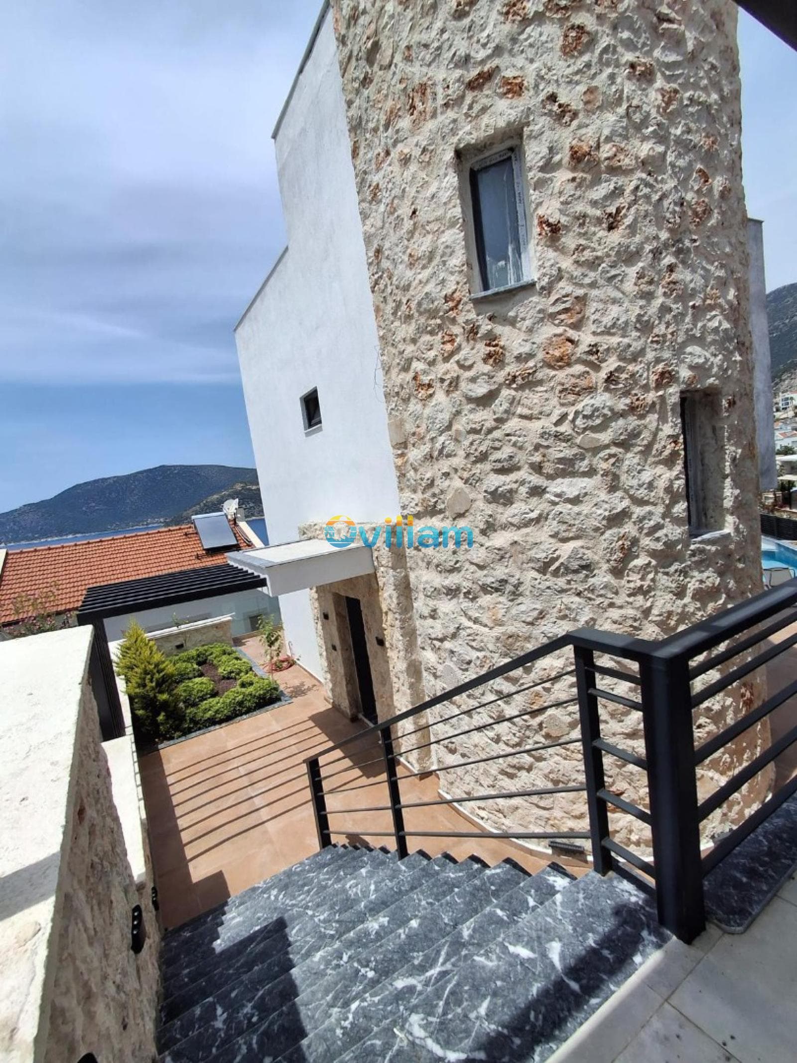 Taş duvarlı villaya çıkan mermer merdivenler ve deniz manzarası.