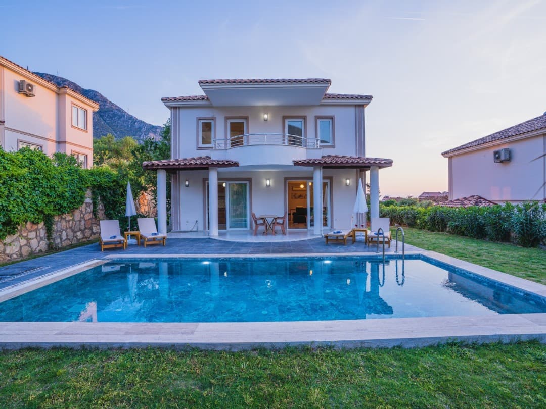 Önünde yüzme havuzu, şezlonglar ve bahçesi bulunan iki katlı müstakil villa.