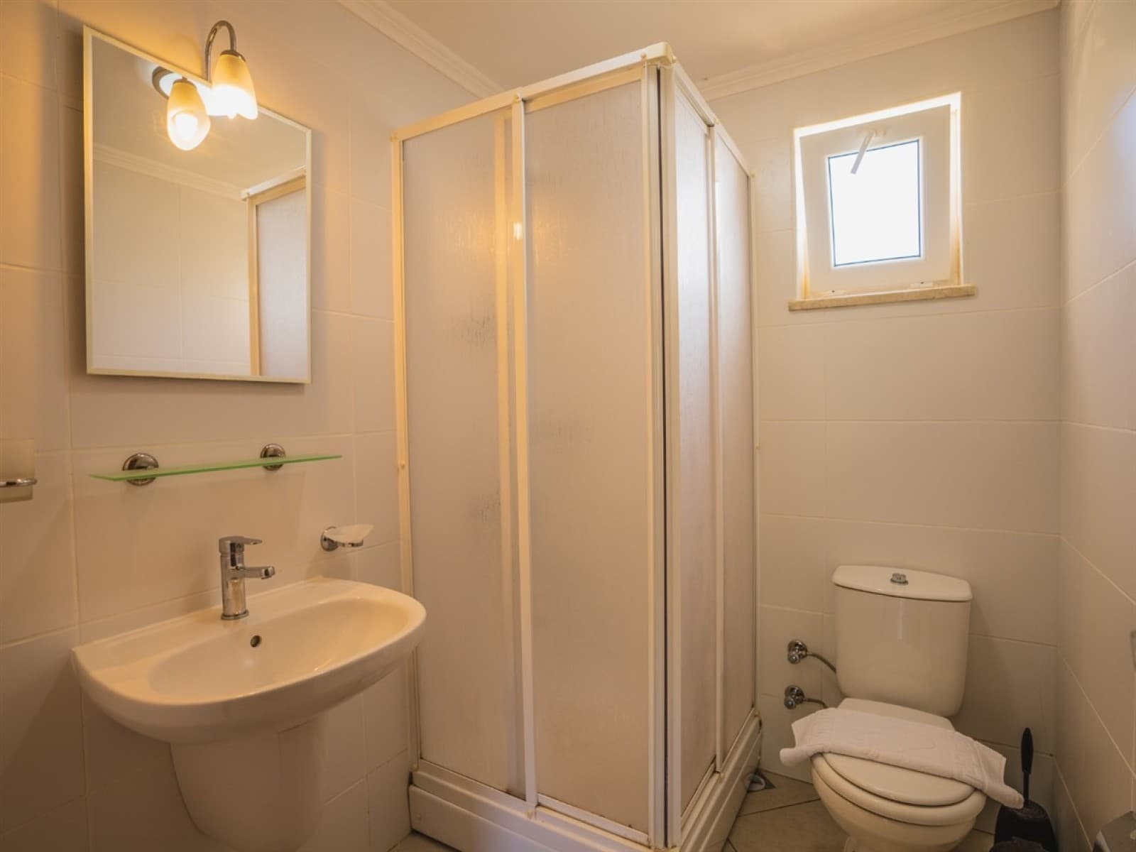 Beyaz fayanslı banyoda duşakabin, lavabo ve tuvalet.