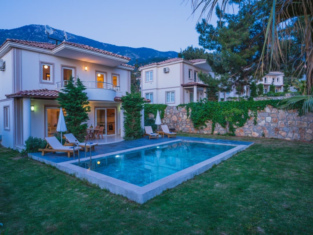 Alacakaranlıkta bahçesinde özel havuzu, şezlongları ve taş duvarı bulunan iki katlı müstakil villa.