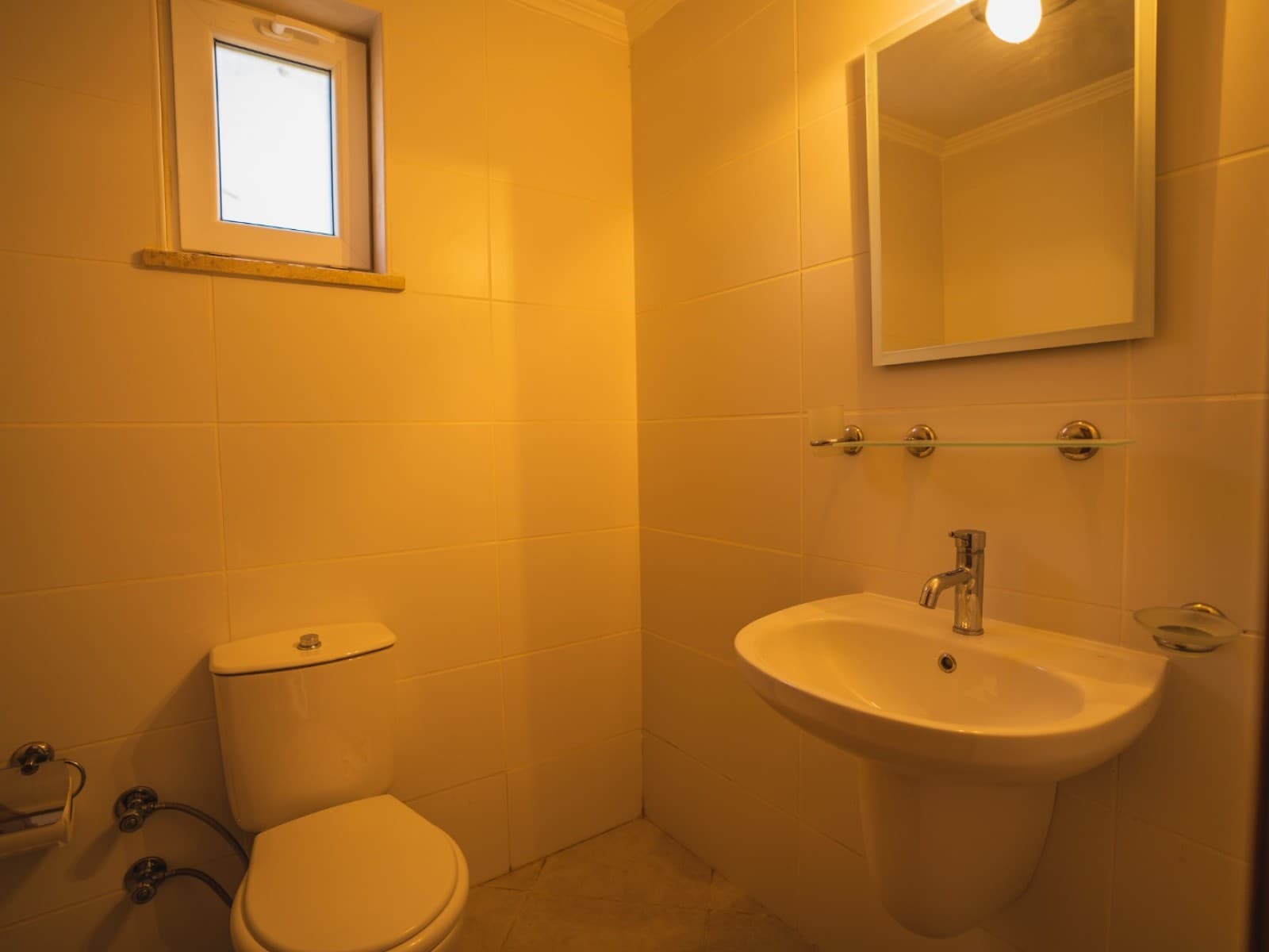 Beyaz seramikli küçük banyo, klozet, ayaklı lavabo ve ayna.