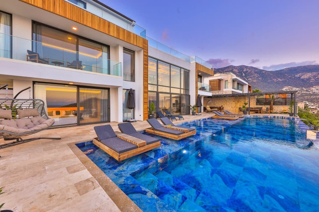 Akşam vakti havuzunda şezlonglar bulunan modern iki katlı lüks villa.