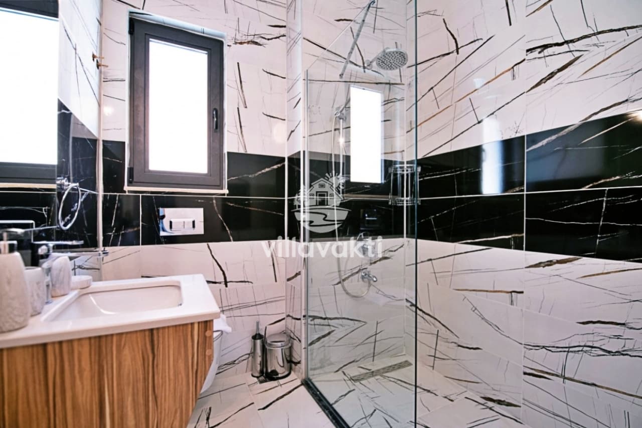Siyah beyaz damarlı mermer kaplı duvarları olan duşakabinli modern banyo.