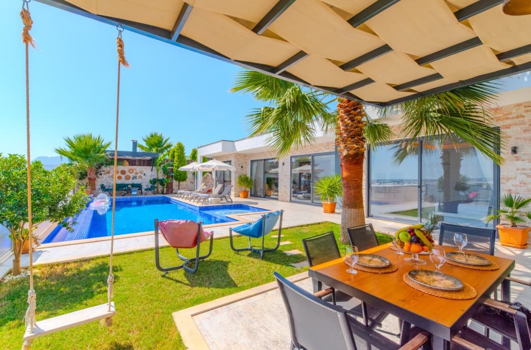 Güneşlikli yemek masası ve salıncak bulunan havuz başı terası.