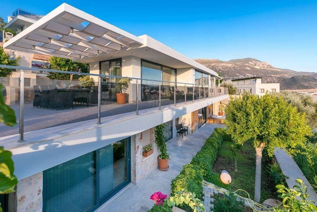 Geniş balkonlu modern villa dış cephesi, dağ manzarası ve yeşil bahçesiyle birlikte.