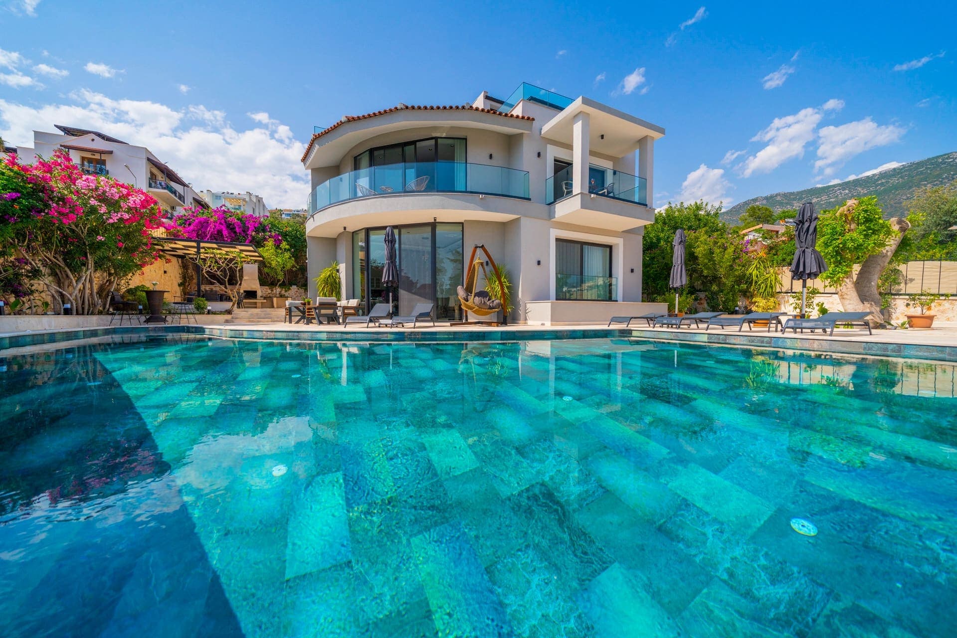 Gündüz vakti havuz ve bahçeyle çevrili iki katlı modern villa dış cephesi.