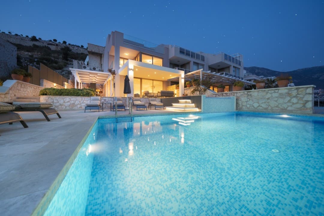 Aydınlatmalı havuz ve şezlonglar önünde iki katlı modern villanın akşam dış cephesi ve yıldızlı gökyüzü.