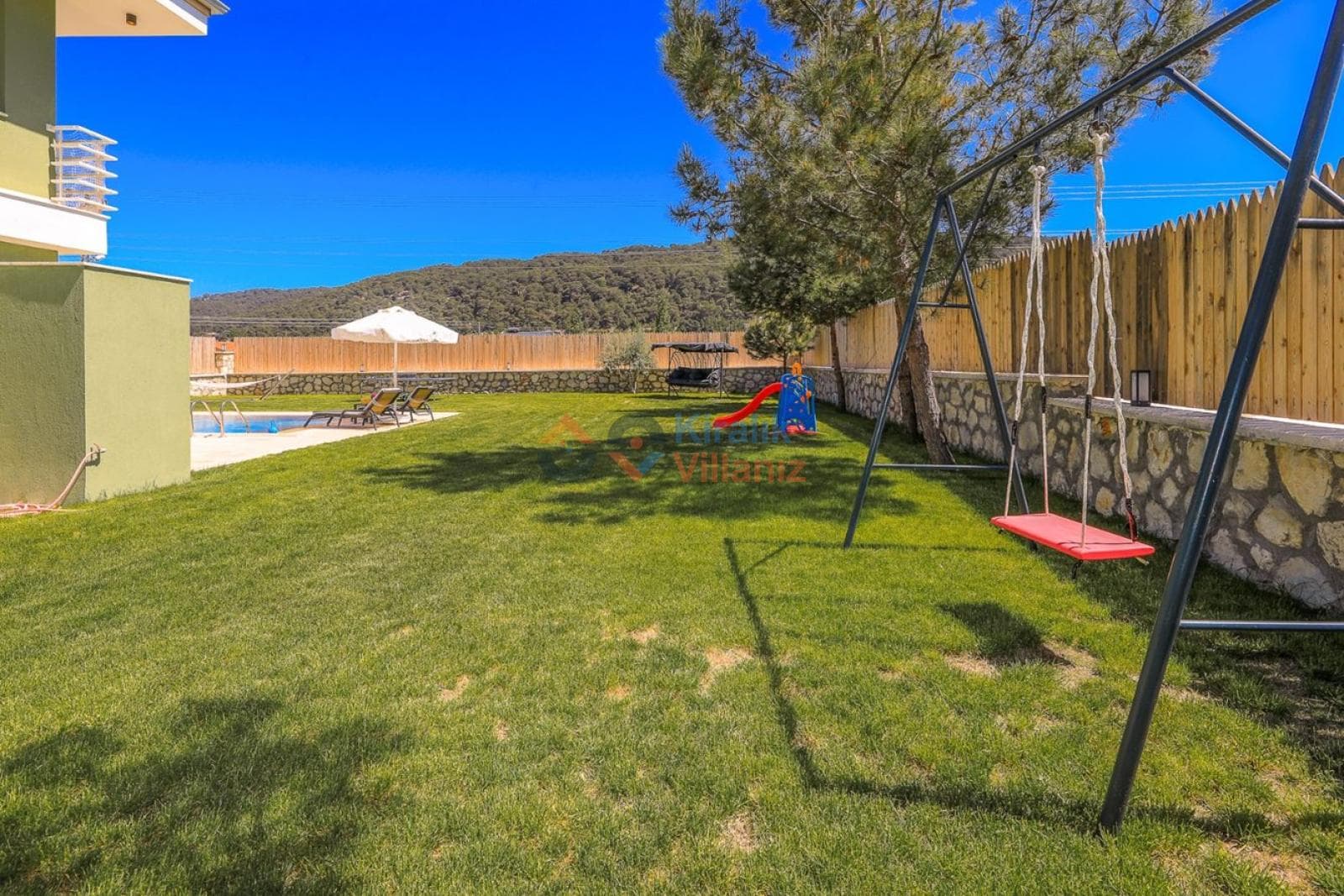 Çim bahçe içinde salıncak ve arka planda havuz bulunan villa bahçesi.
