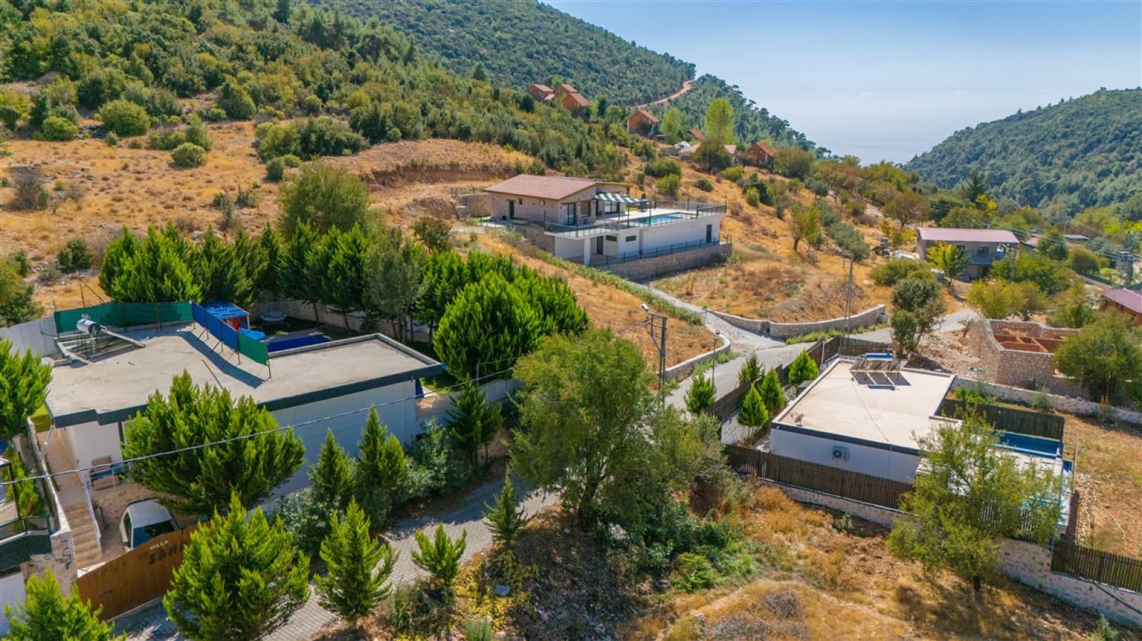 Yeşillikler ve ağaçlar arasında dağ yamacına kurulmuş villaların ve doğanın havadan genel görünümü.