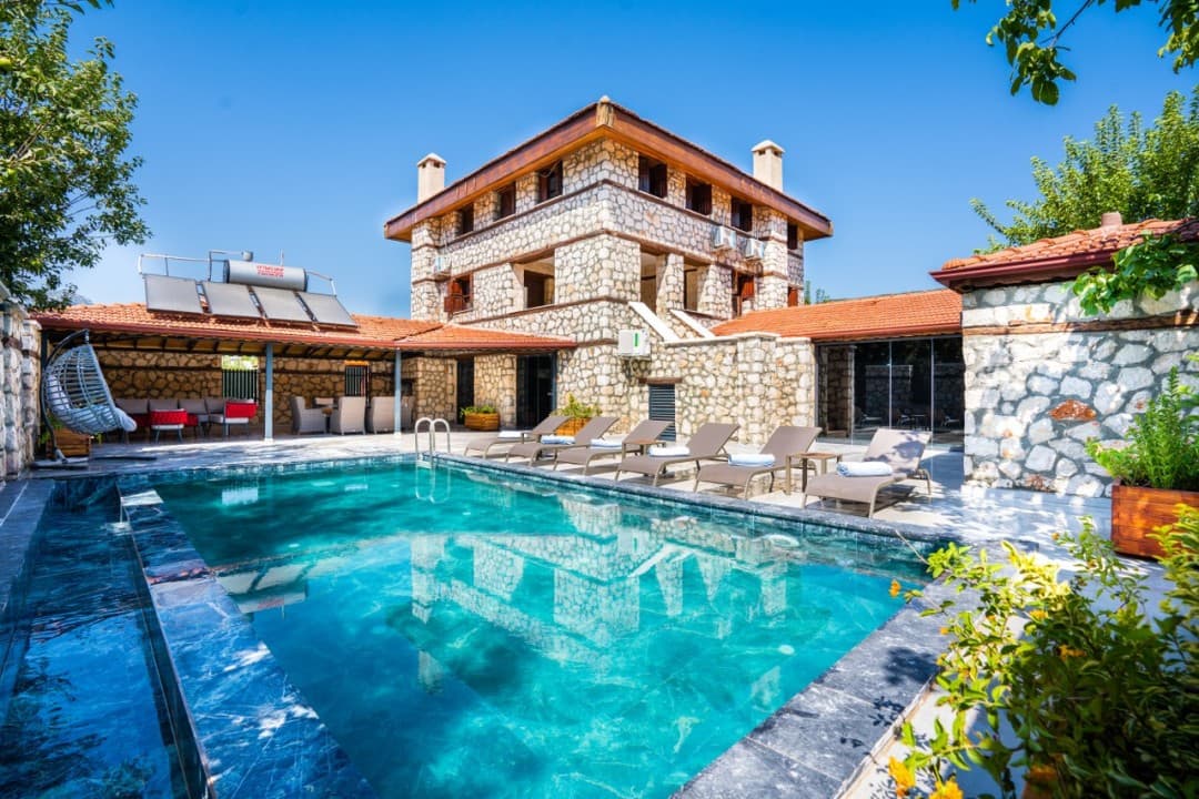 Gündüz vakti taş duvarlı villanın önünde havuz ve şezlonglar yer alıyor.