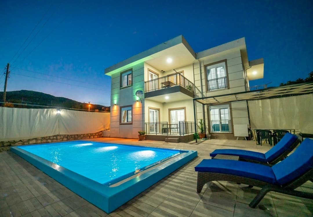 Akşam karanlığında havuzu aydınlatılmış iki katlı müstakil villa.