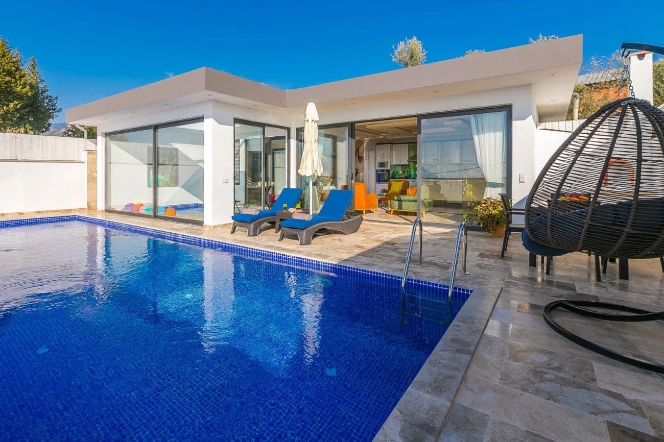 Mavi yüzme havuzu ve şezlongların bulunduğu villanın dış cephesi.