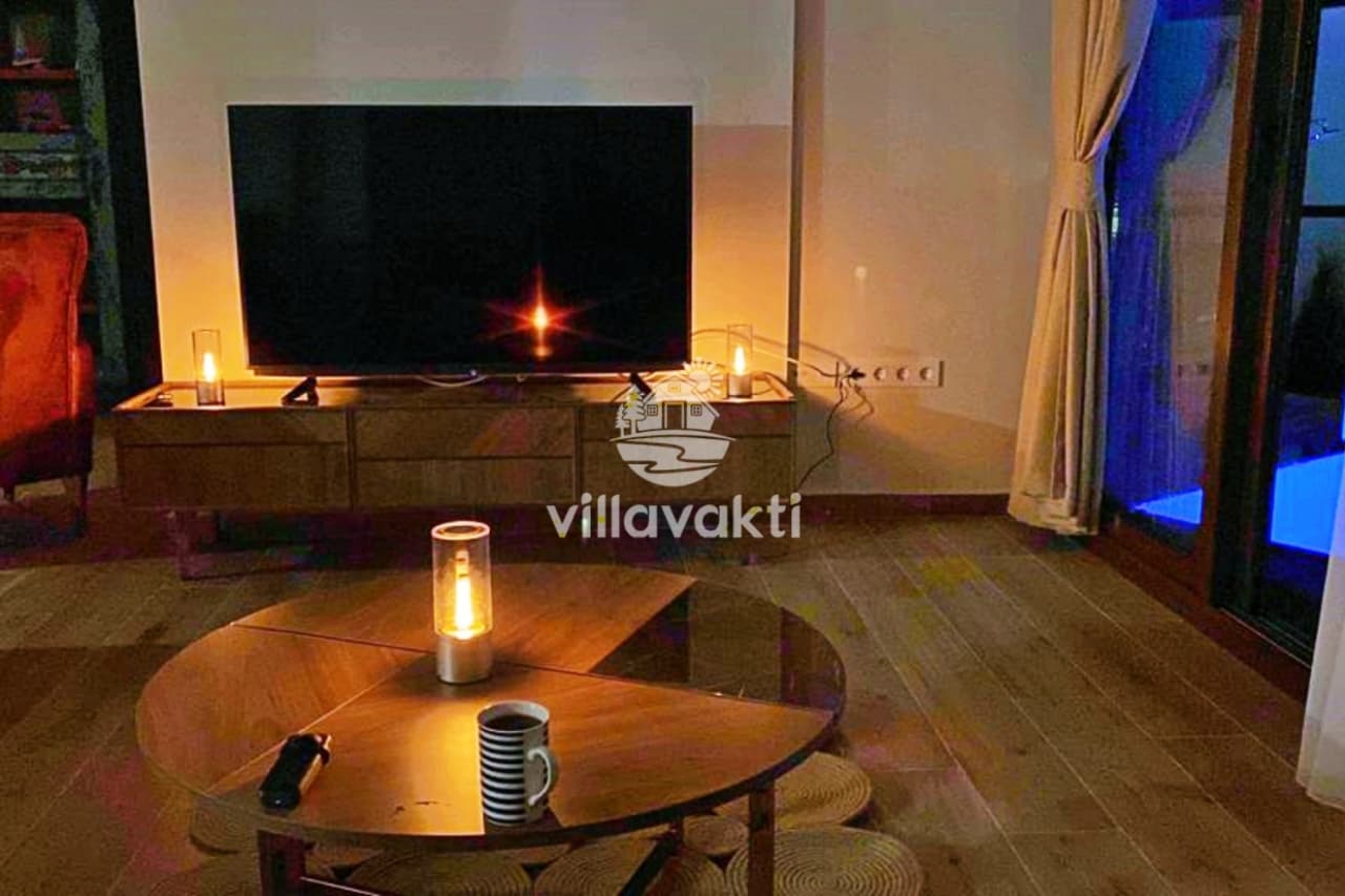 Oturma odasında sehpa üzerinde lambalar ve arkada büyük televizyon.