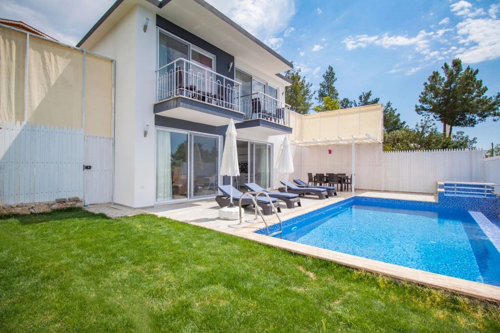 Bahçesinde havuz ve şezlonglar bulunan beyaz cepheli villa.