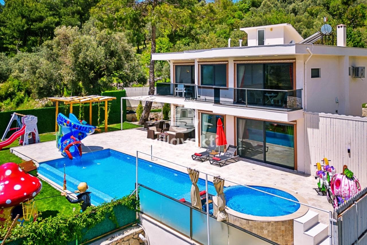 Havuzlu ve kaydıraklı bahçesi olan beyaz villa dış cepheden görünüyor.
