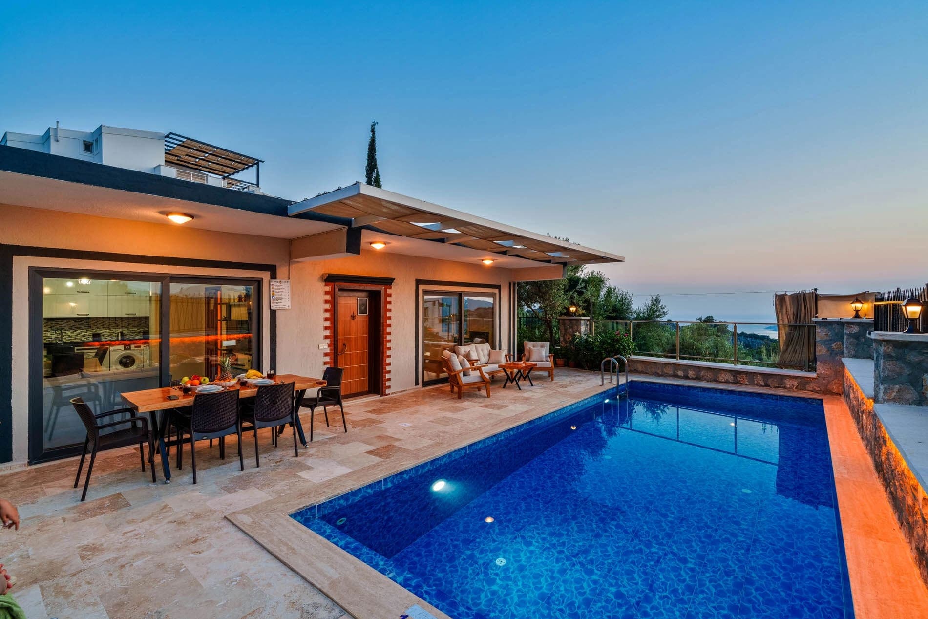 Aydınlatmalı yüzme havuzu ve yemek masası bulunan villa terası.