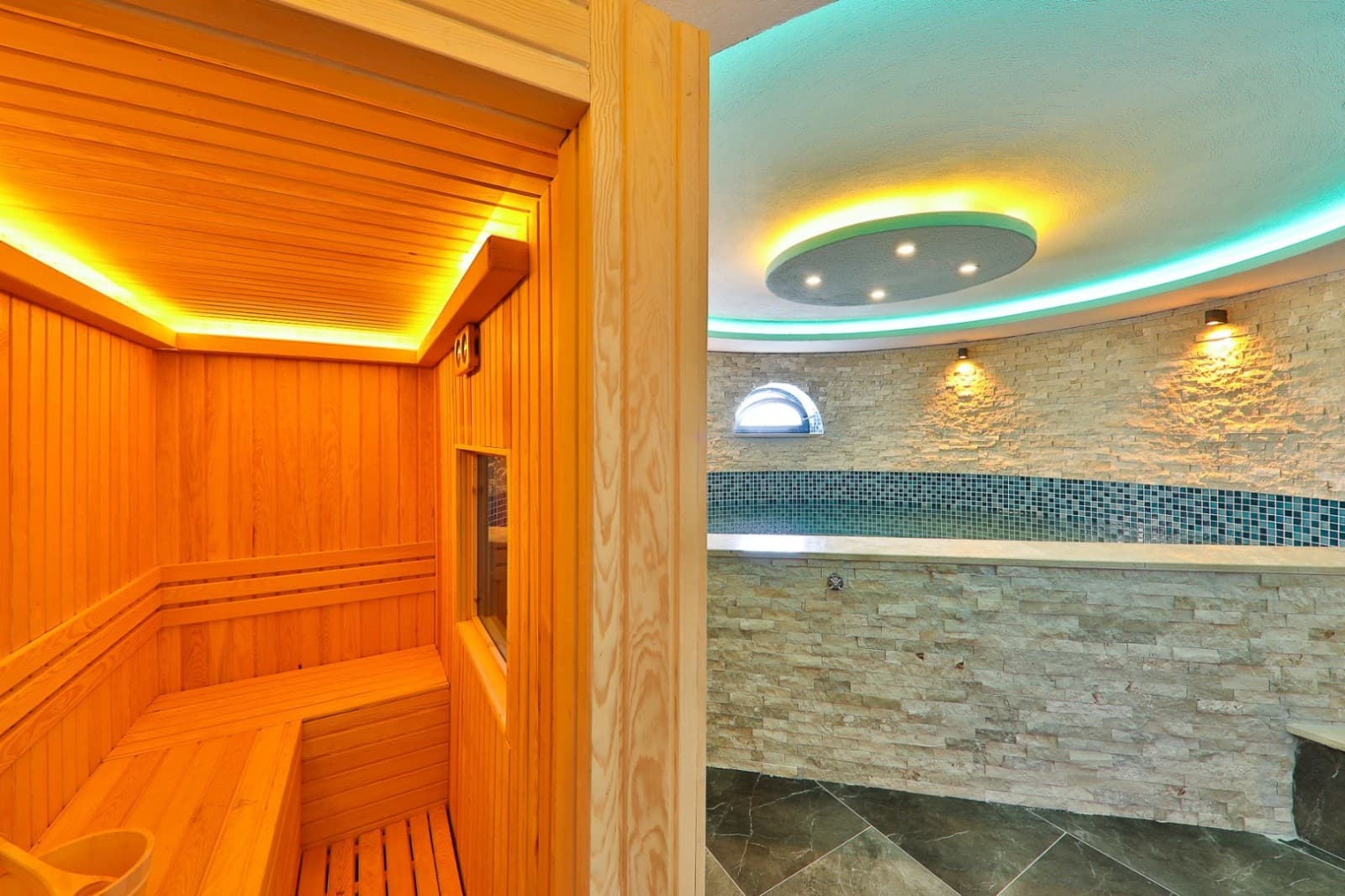 Ahşap kaplamalı sauna odası ve önünde havuz bulunan iç mekân.