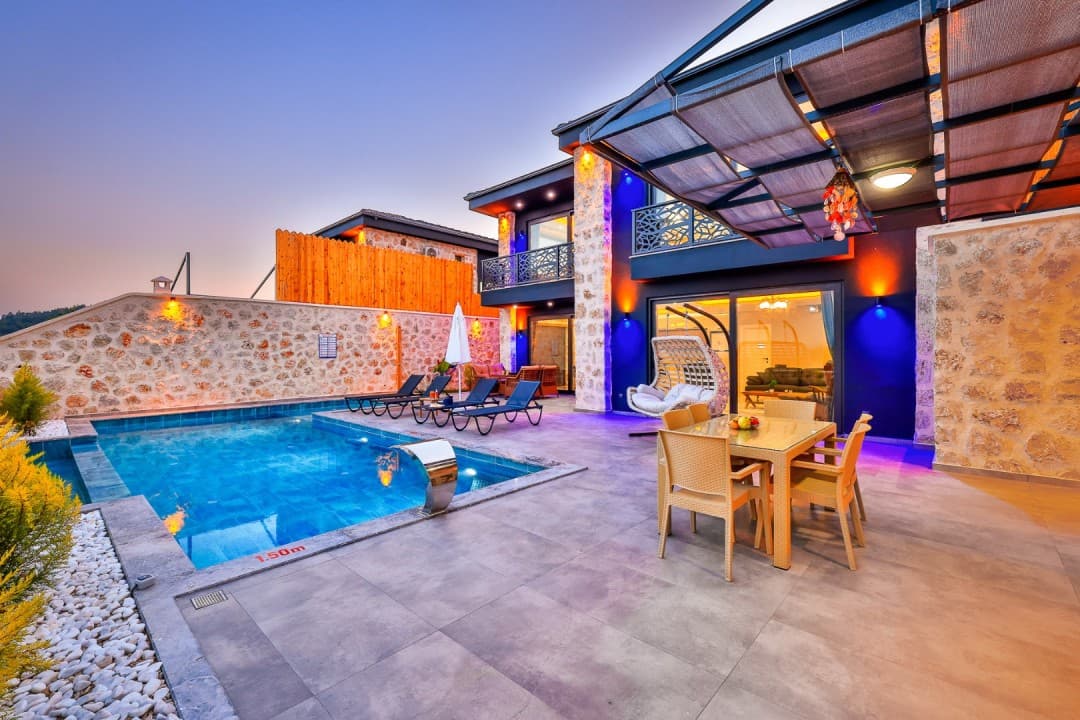 Gün batımında havuzlu, taş duvarlı ve dış aydınlatmalı modern villanın bahçe terası.