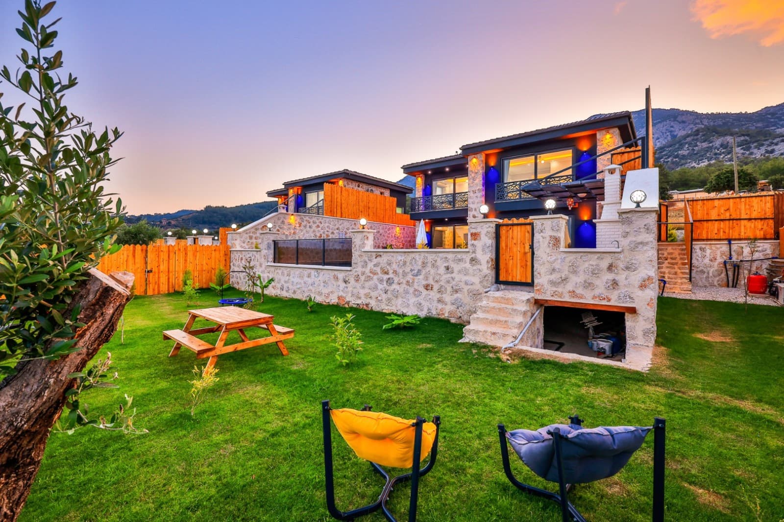 Gün batımında taş duvarlı villa ve çim bahçe.