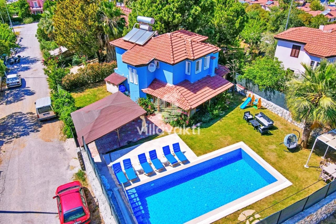 Mavi dış cepheli villanın yüzme havuzu ve şezlonglu yeşil bahçesi.