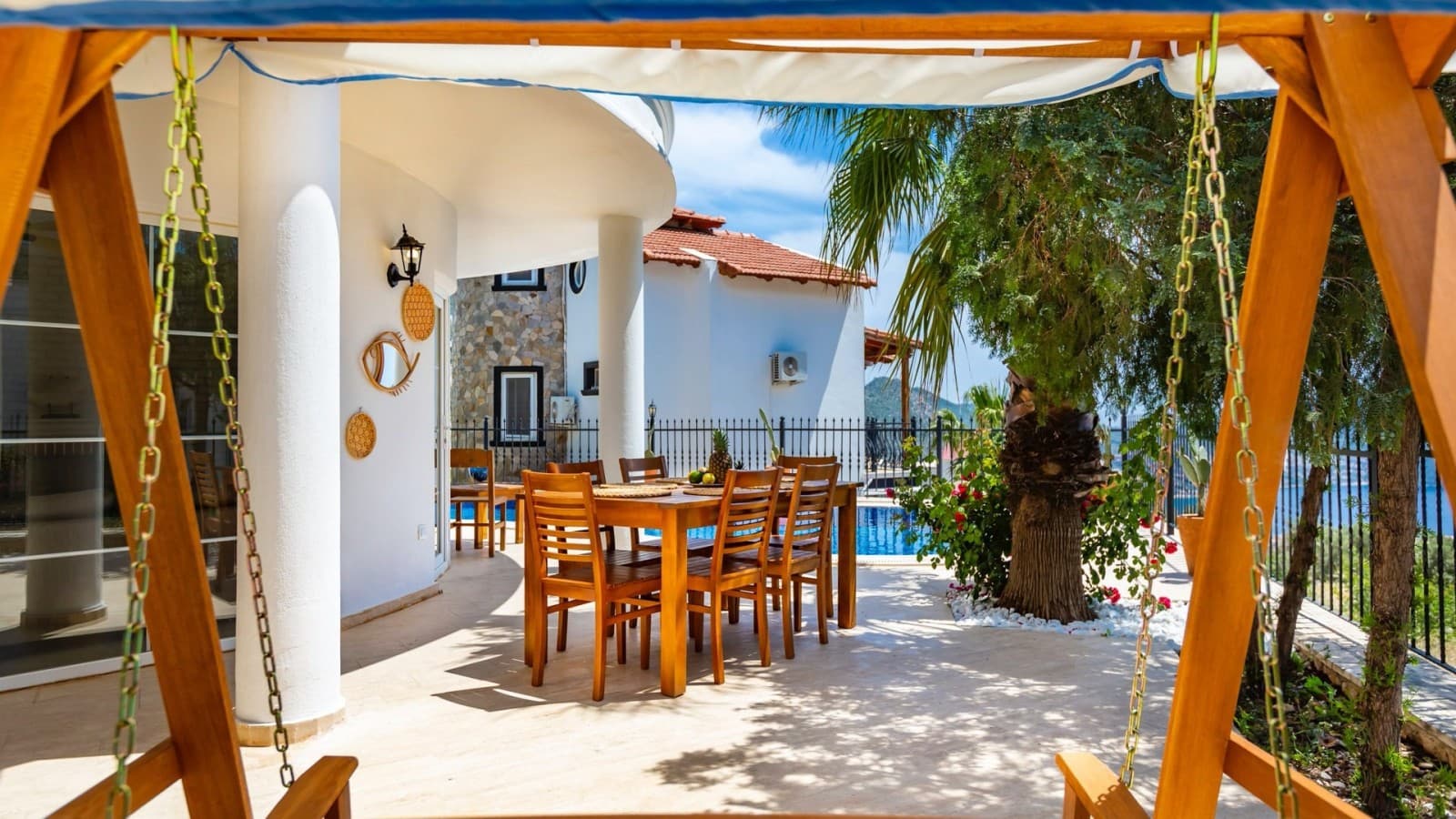Verandada ahşap yemek masası ve ön planda salıncak yer alıyor.