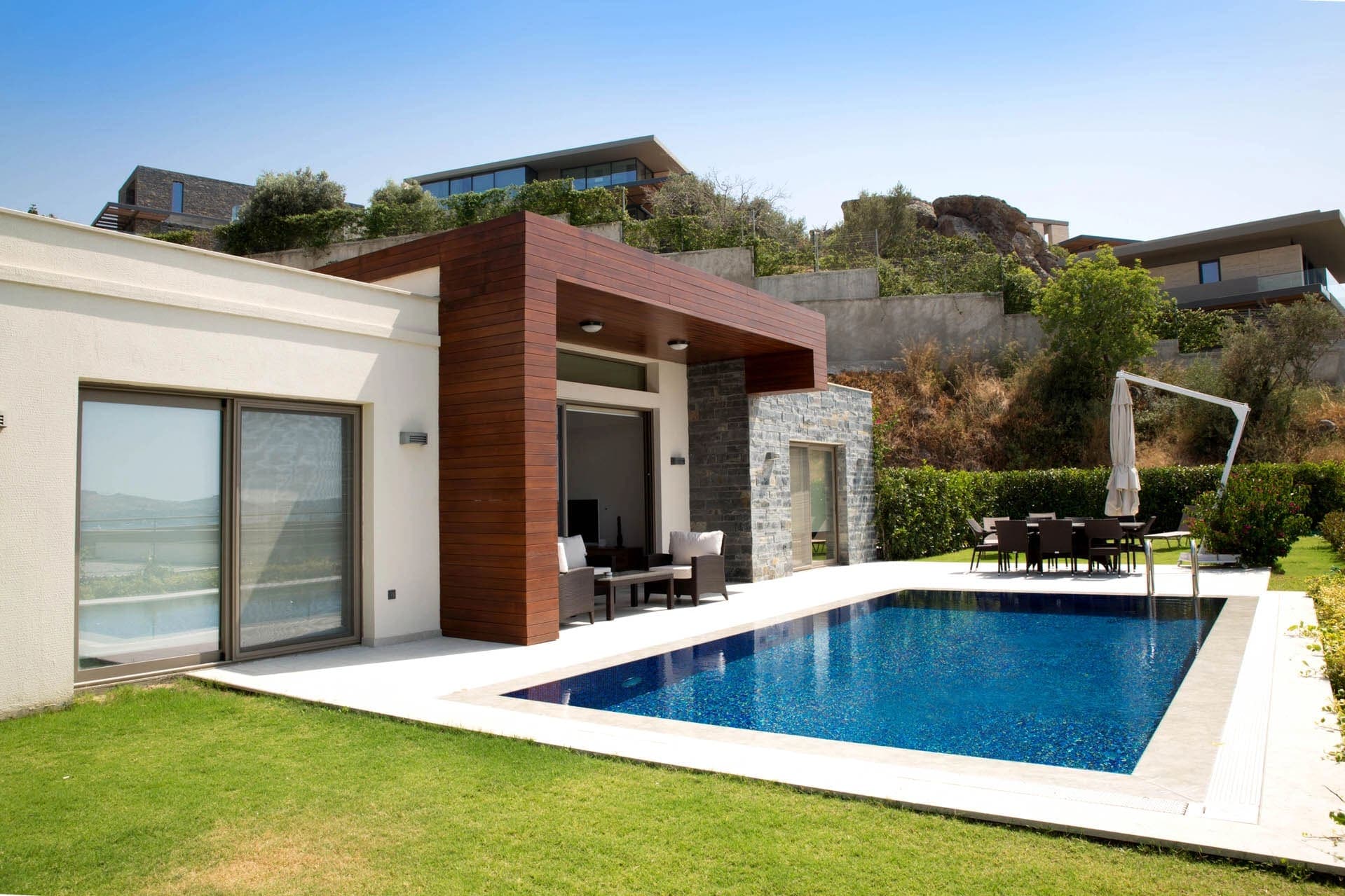 Önünde havuz ve yeşil bahçe olan modern tasarımlı villa dış cephesi.