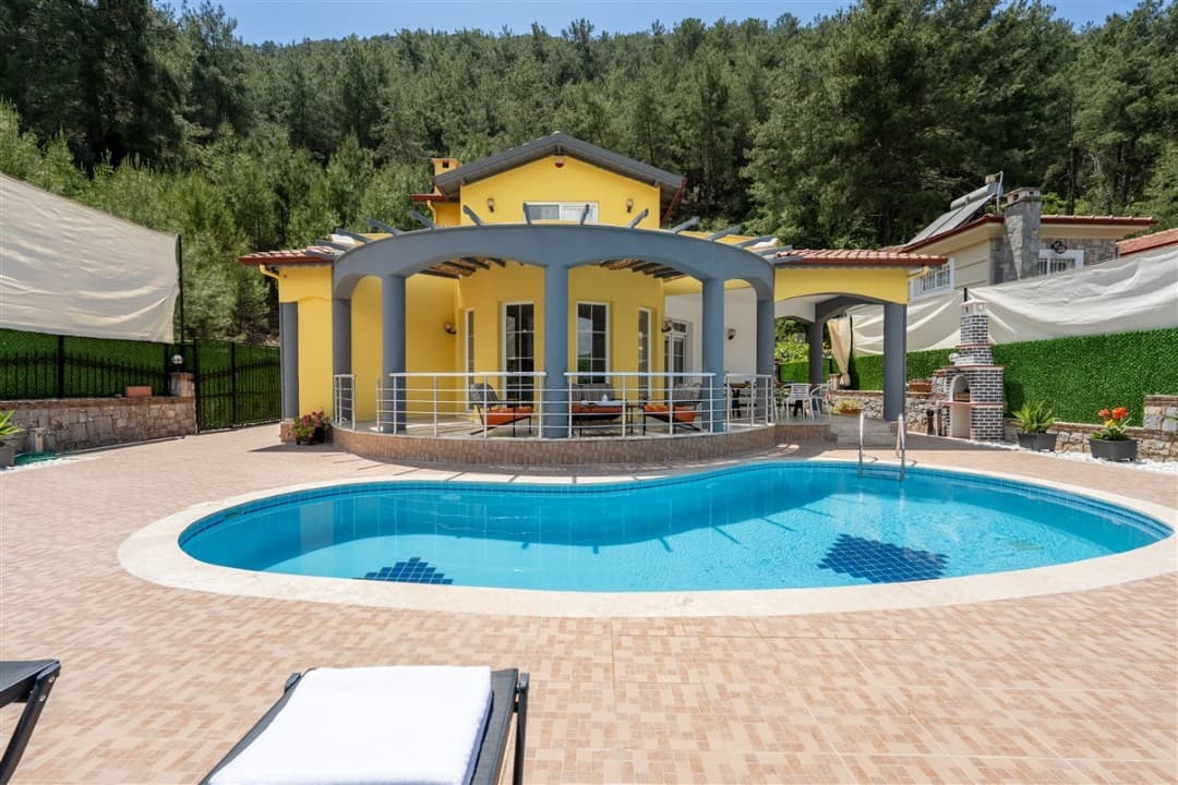 Önünde havuz ve şezlong bulunan sarı dış cepheli iki katlı villa.