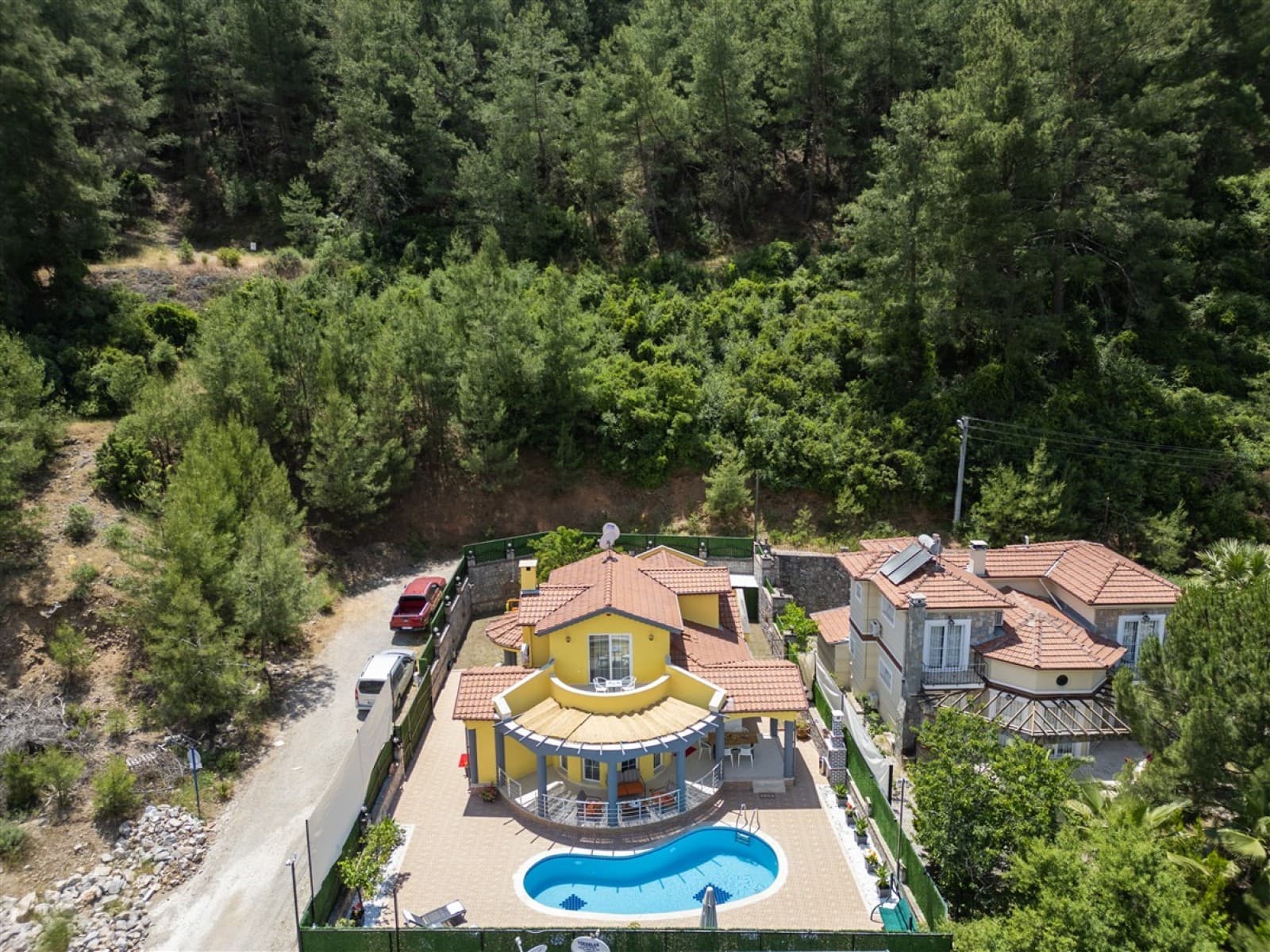 Orman içinde sarı dış cepheli, kiremit çatılı villa ve havuzu.