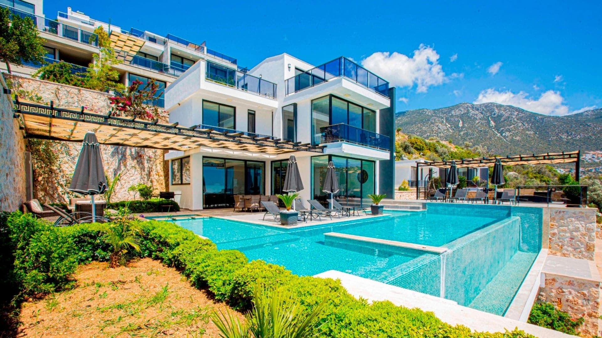 Dağ manzaralı geniş havuzlu lüks beyaz villa dış cephesi.