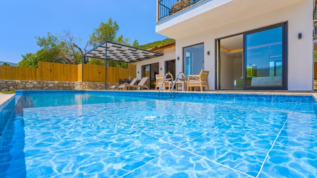 Ön planda havuz ve arkasında beyaz dış cepheli villa.