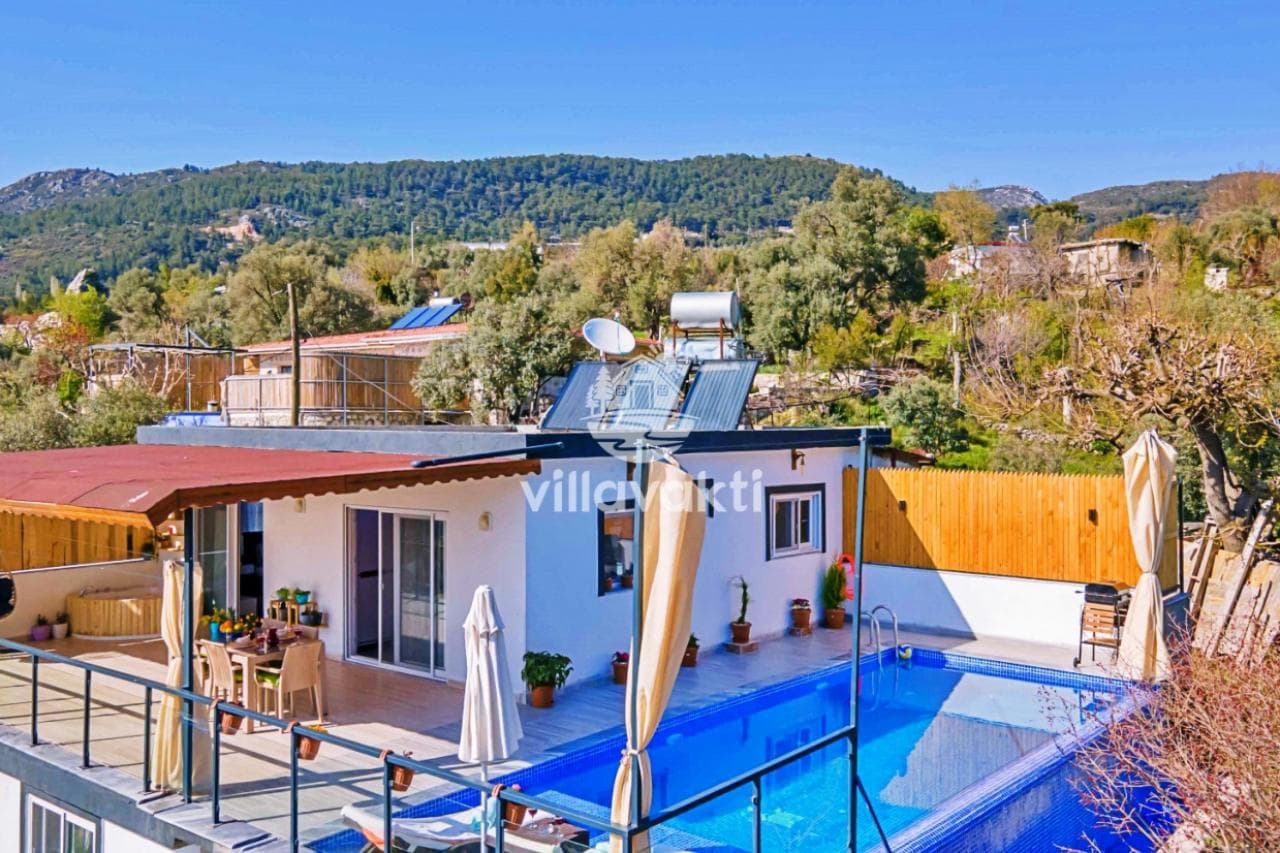 Önünde yüzme havuzu ve şezlonglar bulunan dağ manzaralı villa.
