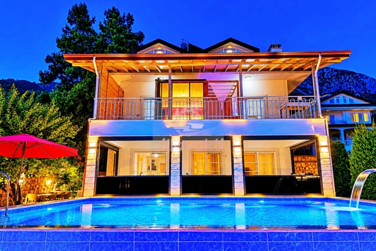 Akşam ışıklandırmalı, önünde havuz bulunan iki katlı villa dış cephesi.