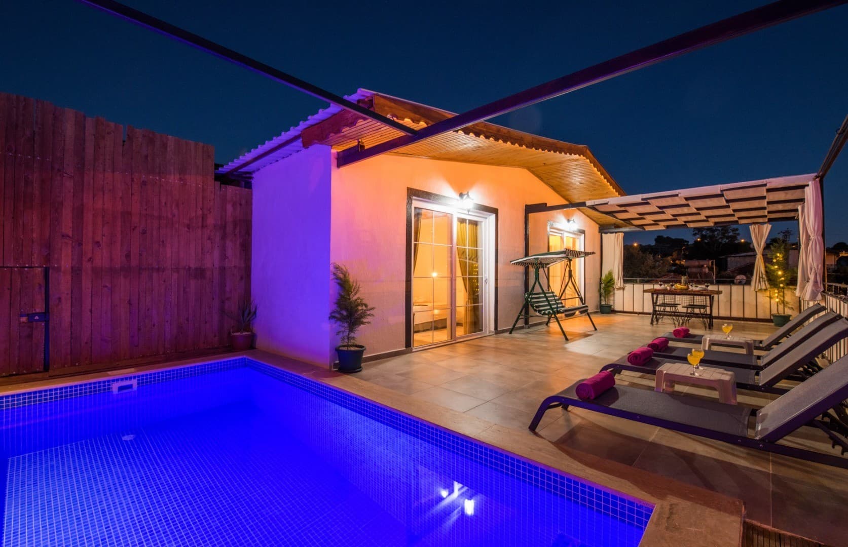 Gece aydınlatmalı özel havuzlu, şezlonglu ve sundurmalı verandaya sahip tek katlı villa.