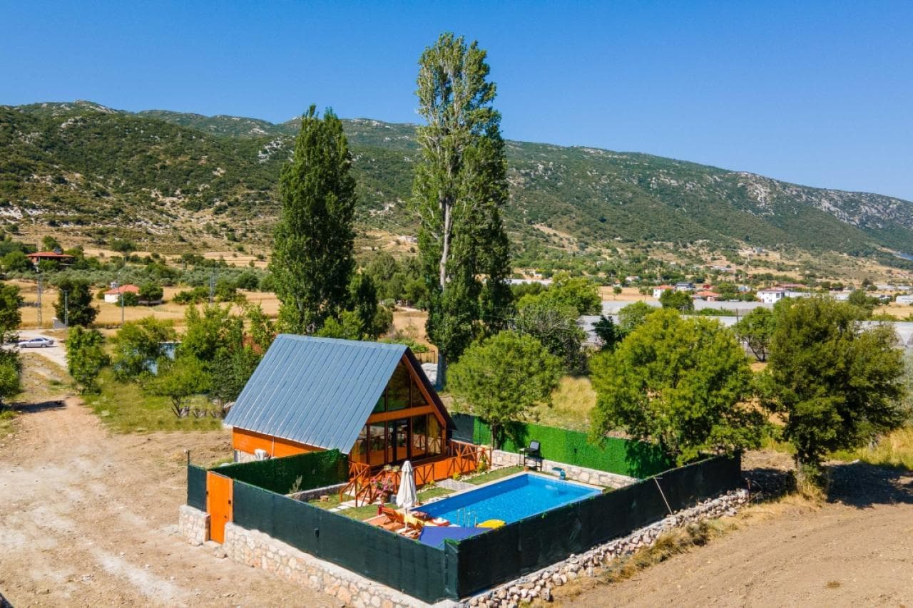 Dağ ve doğa manzarasına bakan, havuzlu ve çitli bahçesi olan ahşap villa.