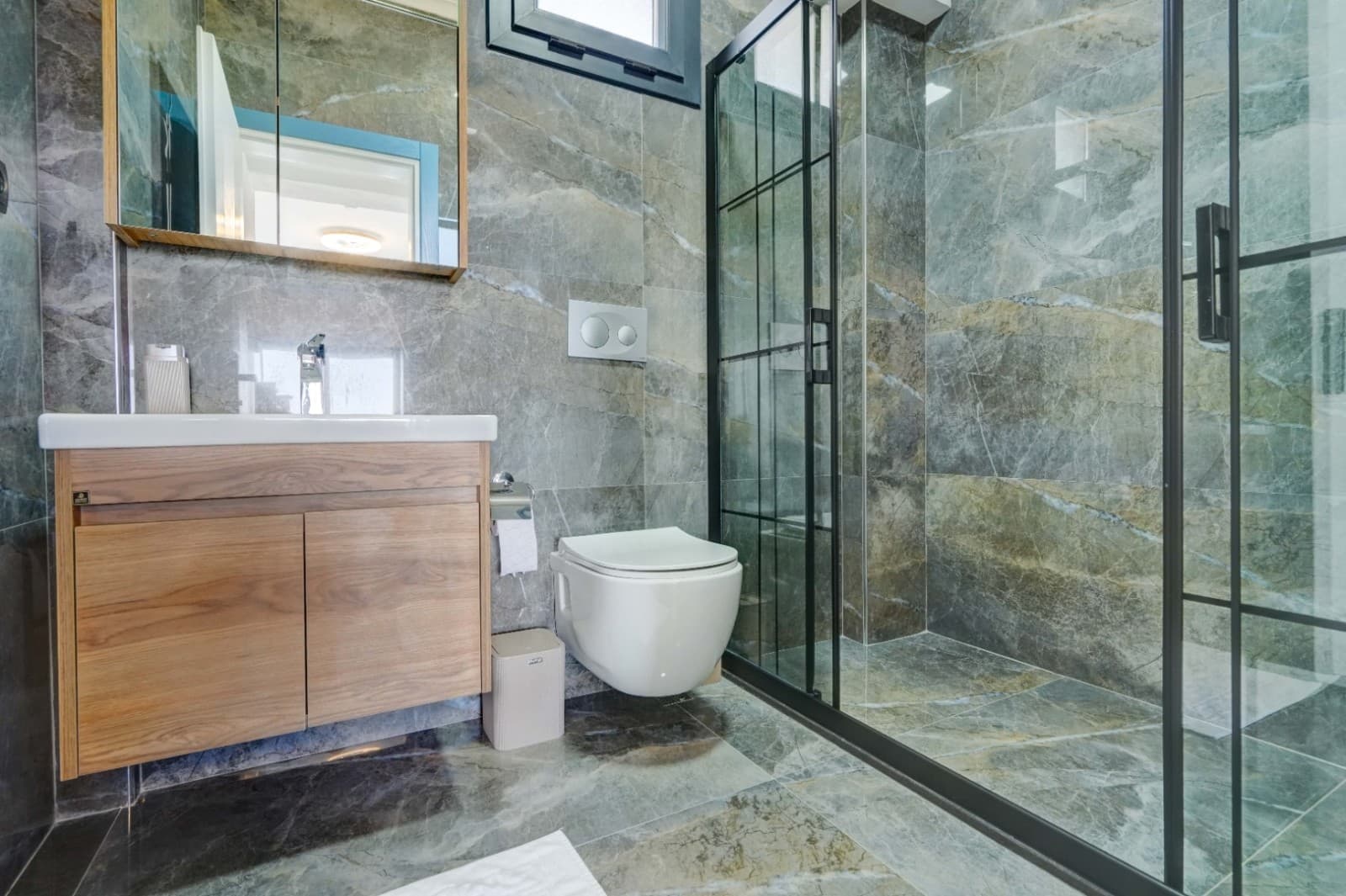 Gri mermer kaplı banyoda duş kabini ve ahşap dolaplı lavabo.