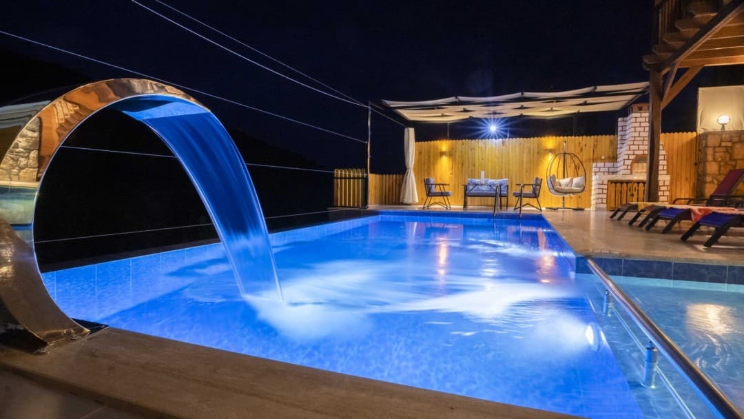 Gece havuz şelalesi ve aydınlatmalı havuz kenarı oturma alanı.
