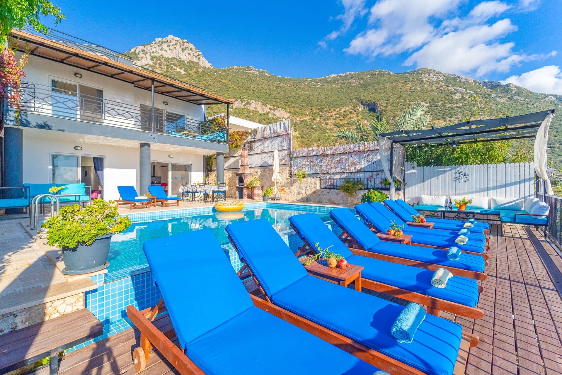 Dağ manzaralı havuz kenarında mavi şezlonglar ve iki katlı villa.