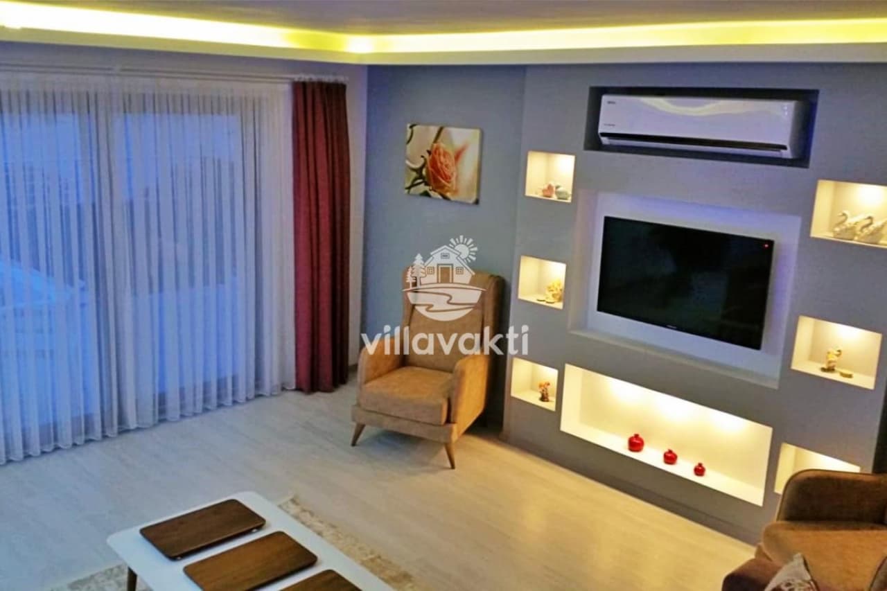 Gri duvarlı, televizyon üniteli ve tekli koltuk bulunan oturma odası.