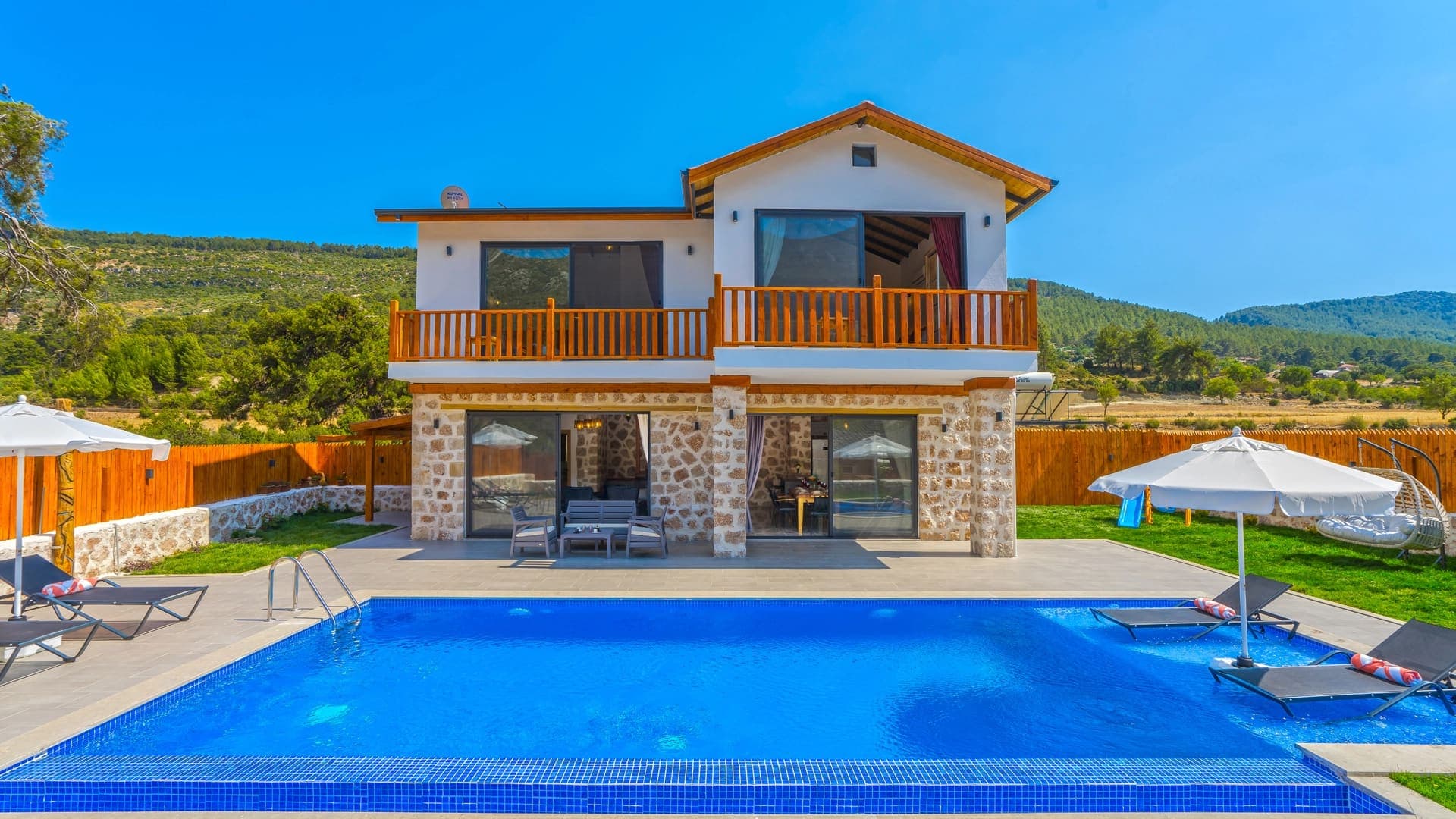 Bahçesinde havuz ve şezlonglar bulunan iki katlı taş villa.