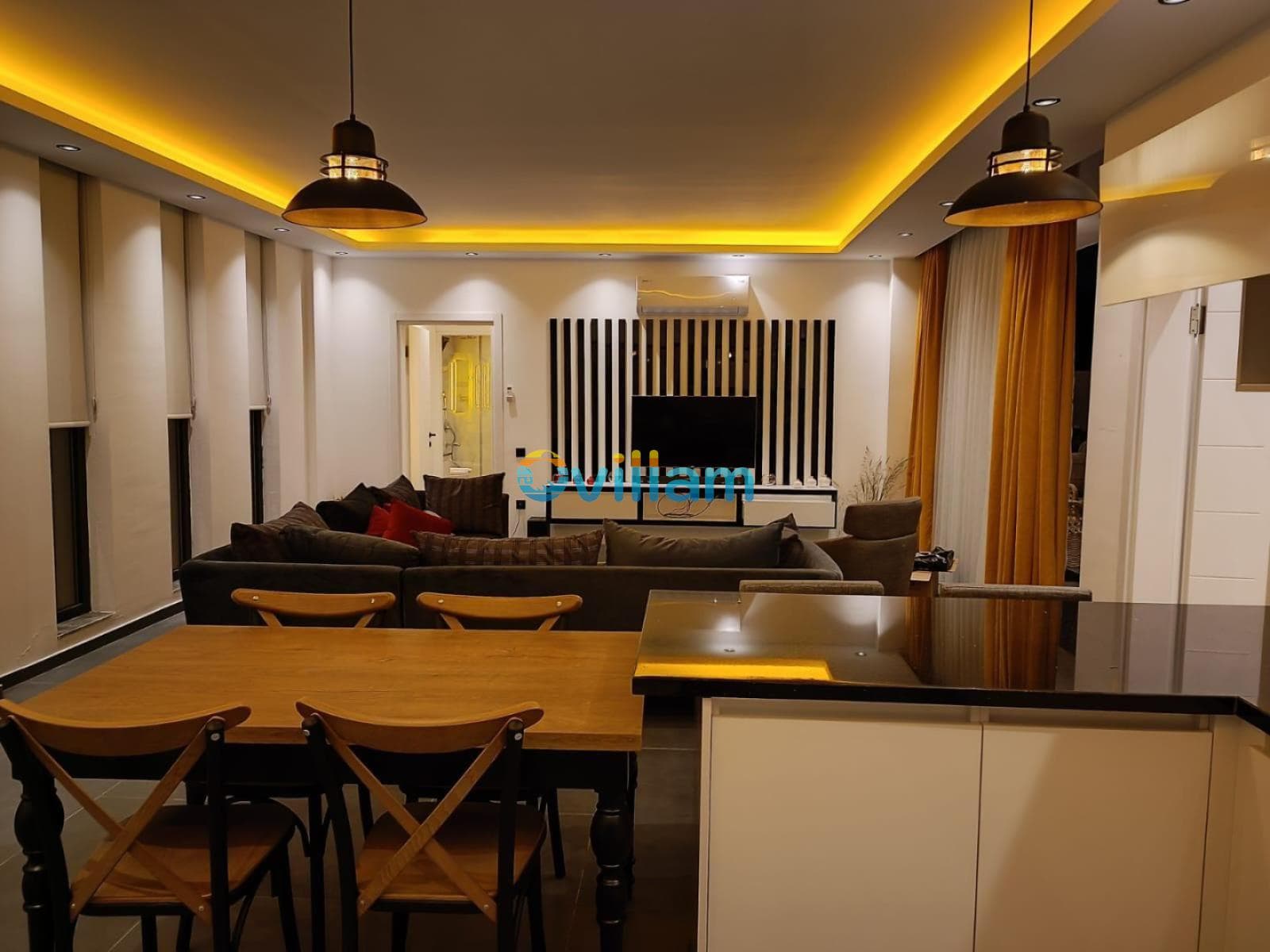 Ahşap yemek masası ve arkasında modern oturma grubu bulunan salon.