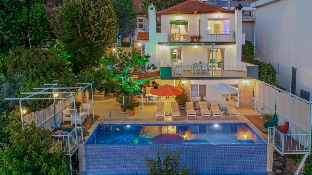 Akşam vakti havuz başı şezlongları ve aydınlatmalı iki katlı villa.