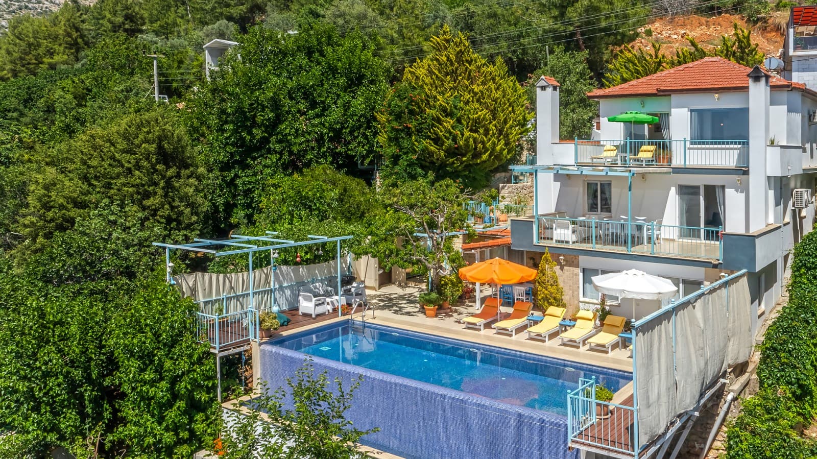 Yeşillikler içinde havuzu ve çok katlı balkonları bulunan beyaz dış cepheli villa.
