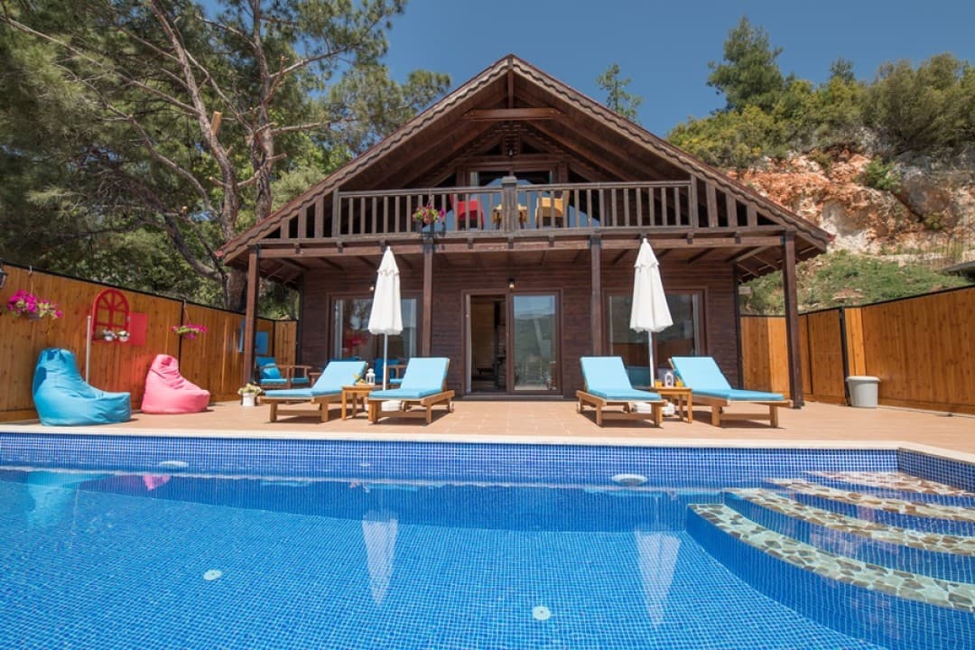 Önünde havuz ve şezlonglar bulunan, ahşap iki katlı villa.