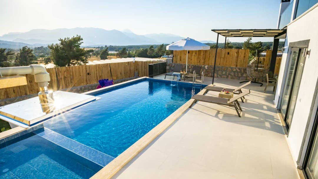 Dağ manzaralı, özel yüzme havuzlu, şezlong ve güneş şemsiyesi bulunan villa terası.