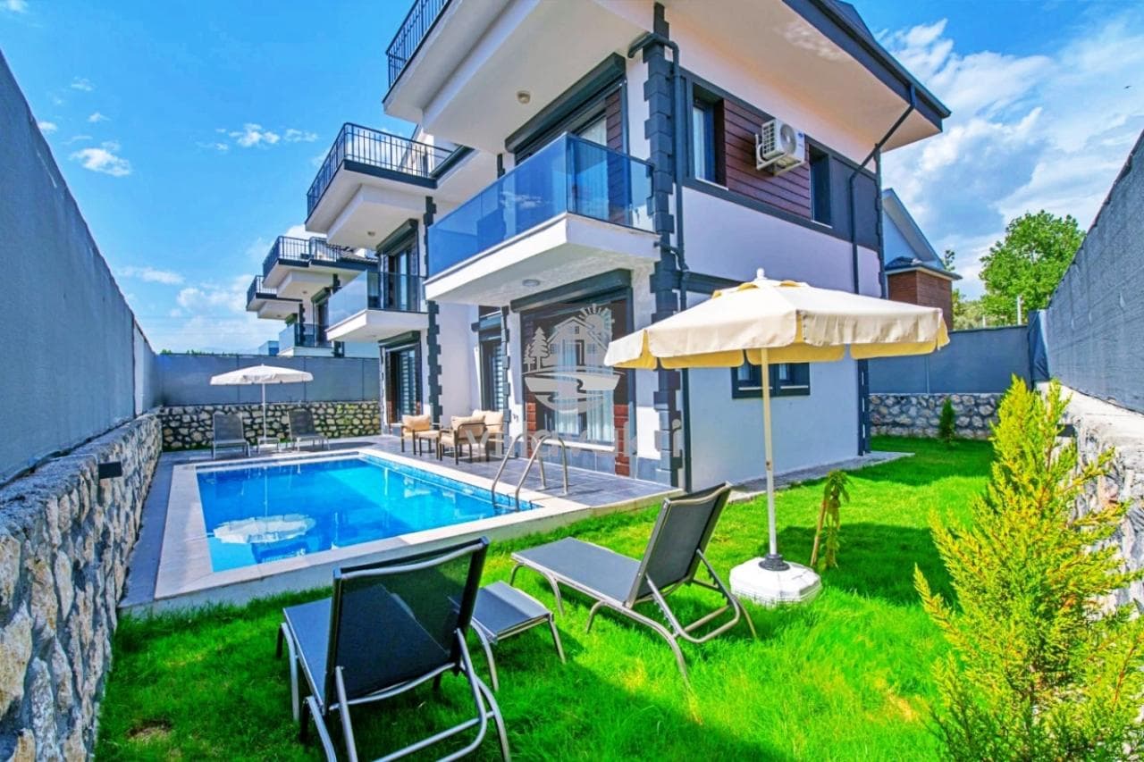 Bahçesinde havuz ve şezlonglar bulunan iki katlı villa.